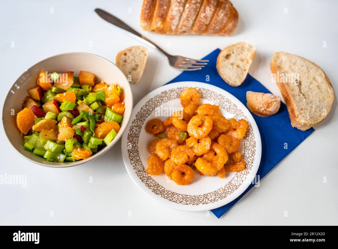 Gamberetti fritti, insalata di frutta, pane e forchetta su tovagliolo blu su sfondo bianco. Foto Stock