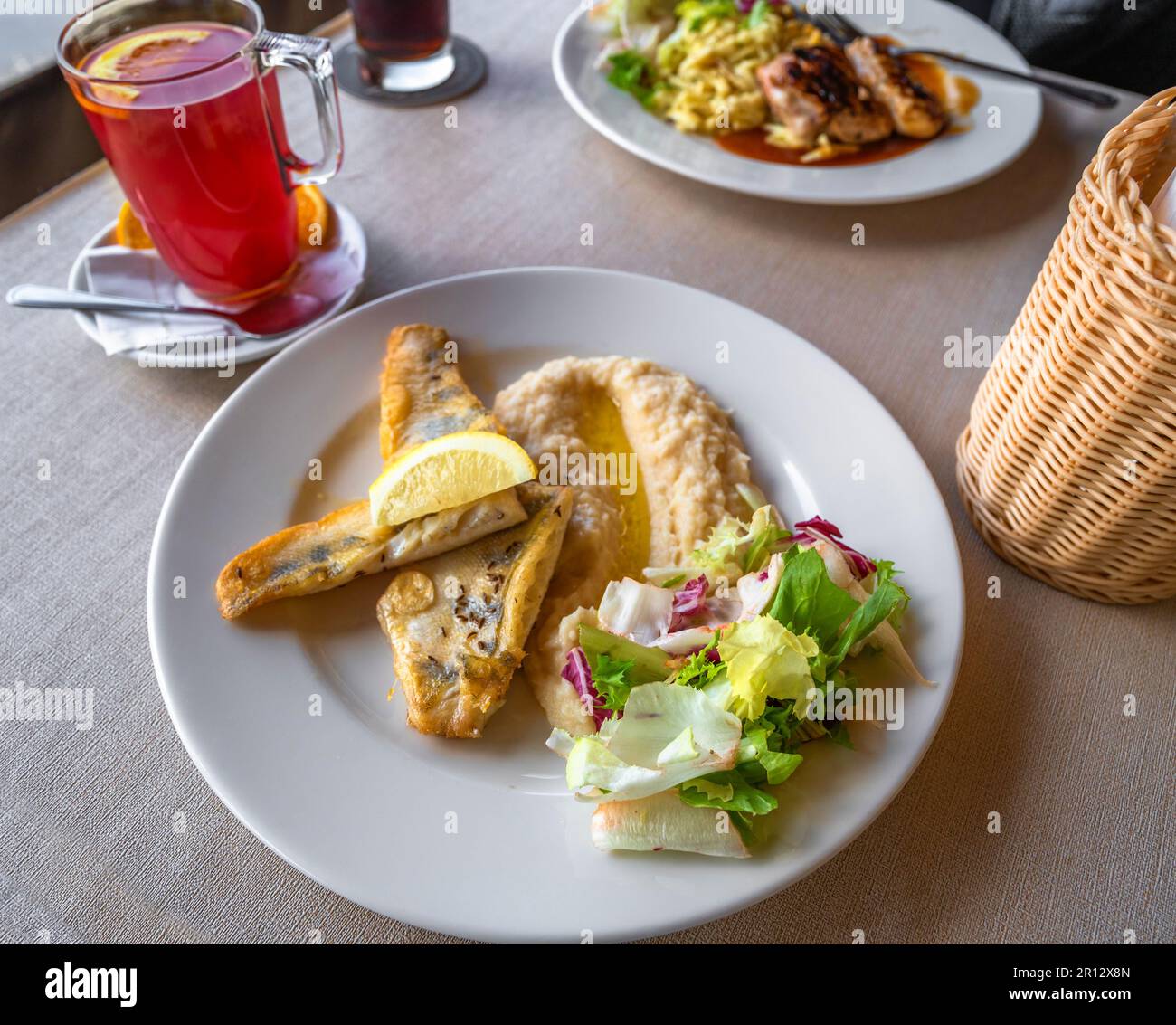 Primo piatto con filetto di zander con purea di ceci e prezzemolo, secondo con spätzle, tè alla frutta e cesto al tavolo del ristorante. Foto Stock