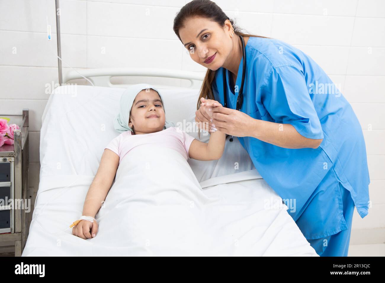 Giovane donna indiana infermiera o medico che tiene la mano di bambina paziente cancro sdraiato sul letto di ospedale in corso di chemioterapia. Aspetto Foto Stock