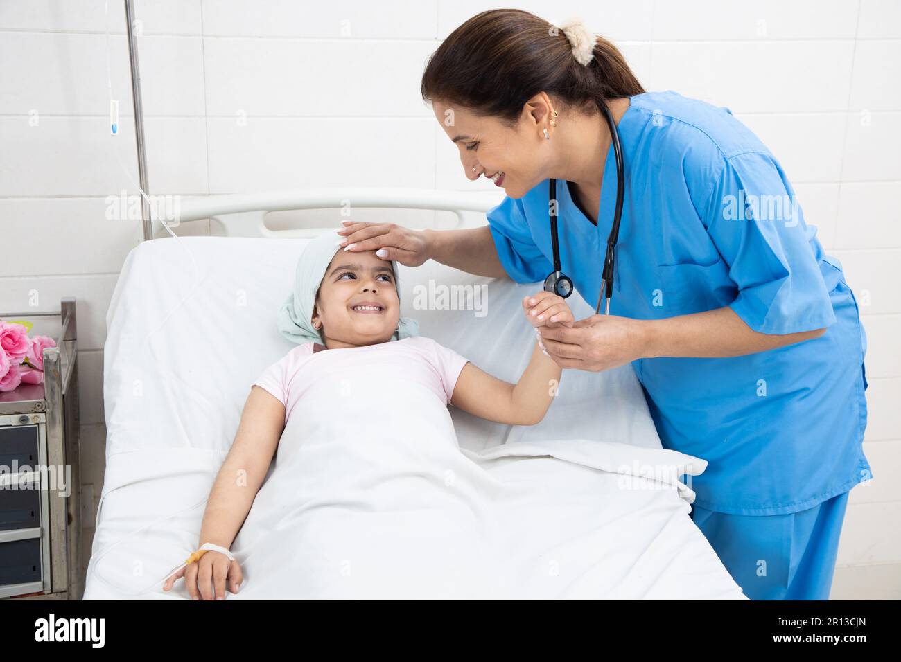 Giovane donna indiana infermiera o persona medica visita e controllo bambina paziente cancro sdraiato sul letto di ospedale in corso di chemioterapia. Healt Foto Stock