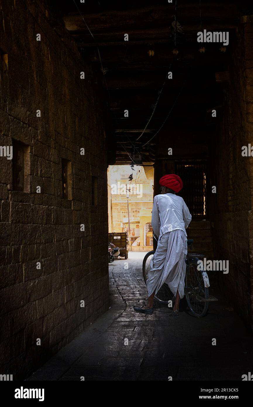 Uomo indiano in abiti tradizionali che cammina con la sua bicicletta attraverso un passaggio buio Foto Stock