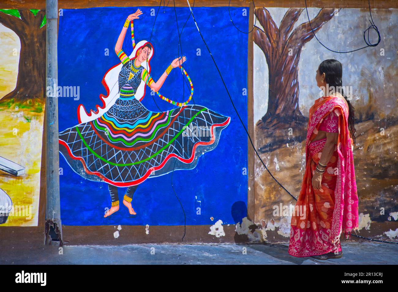 Una donna indiana in sari camminando vicino a una bella pittura murale che rappresenta una ballerina Foto Stock