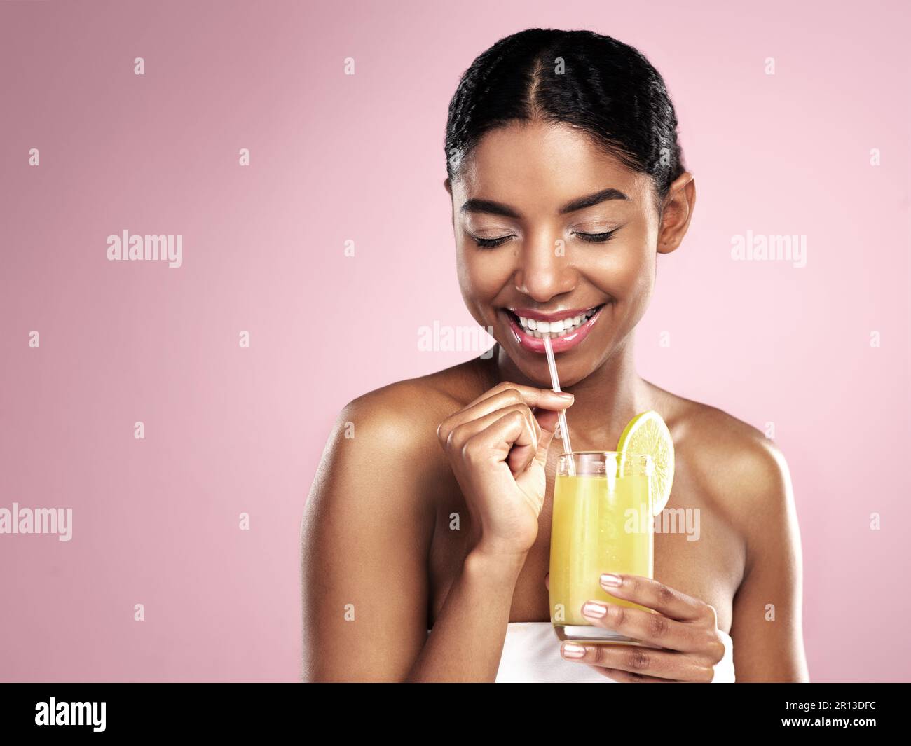 Felice donna bere un bicchiere di succo d'arancia in studio, sfondo rosa e mockup per una sana cura della pelle. Modello africano, cocktail di frutta e frullato per Foto Stock
