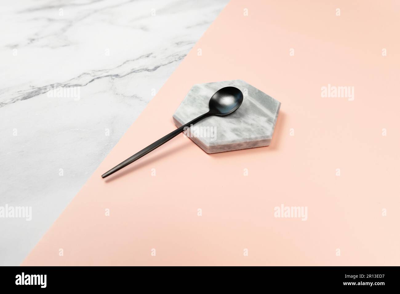 Cucchiaio da dessert nero su fondo in marmo. Marmo bianco e sfondo rosa. Posate nere, spazio copia. Foto Stock