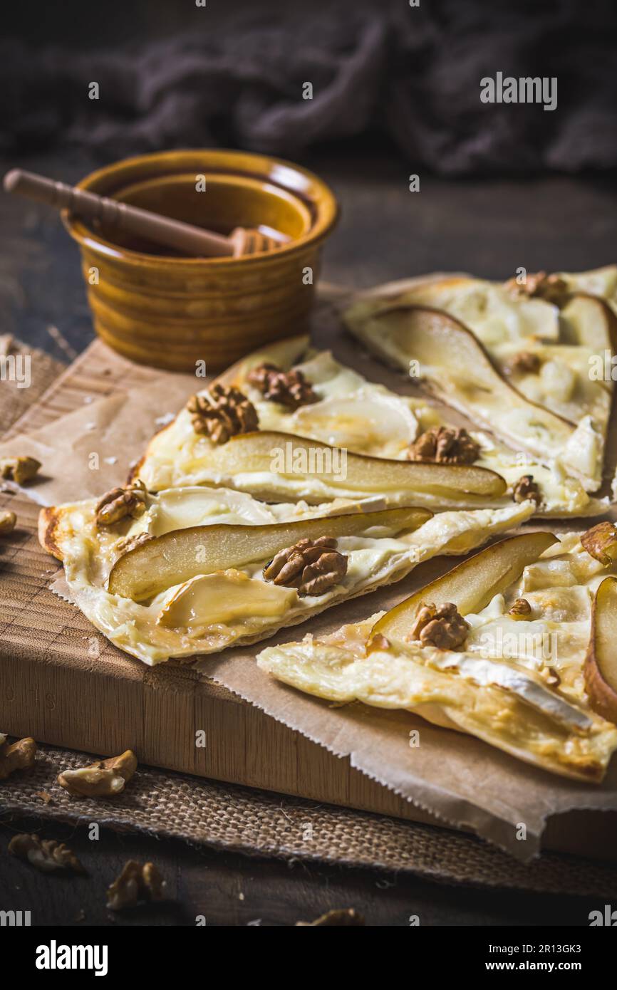 Tarte flambee con pera, formaggio di capra, miele e noci su fondo di legno rustico scuro, verticale Foto Stock