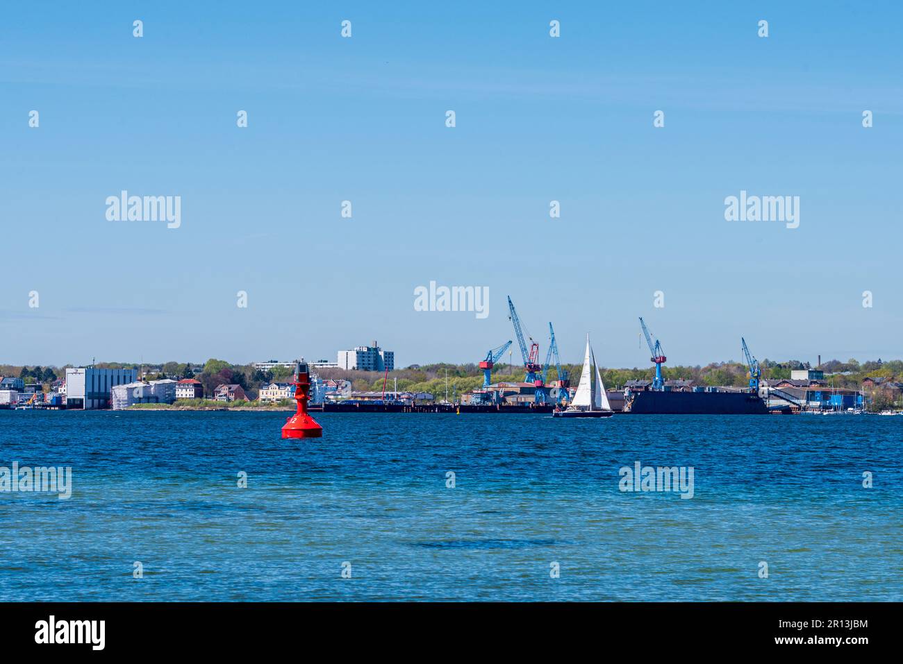 Kiel, Deutschland, mai 2023 Blick über die Innenförde nach Friedrichsort mit der Werft eine Segelyacht fährt vorbei im Vordergrund eine rote Fahrwasse Foto Stock
