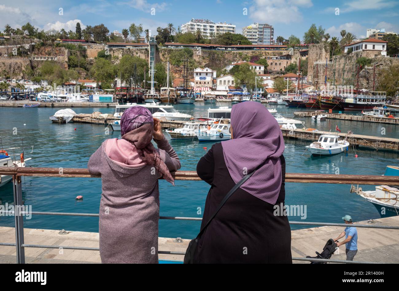 Due donne che indossano hijab islamici, o velo, si appoggiano sulle ringhiere mentre si affacciano sull'antico porto di Kaleici ad Antalya, in Turchia (Turkiye). Foto Stock