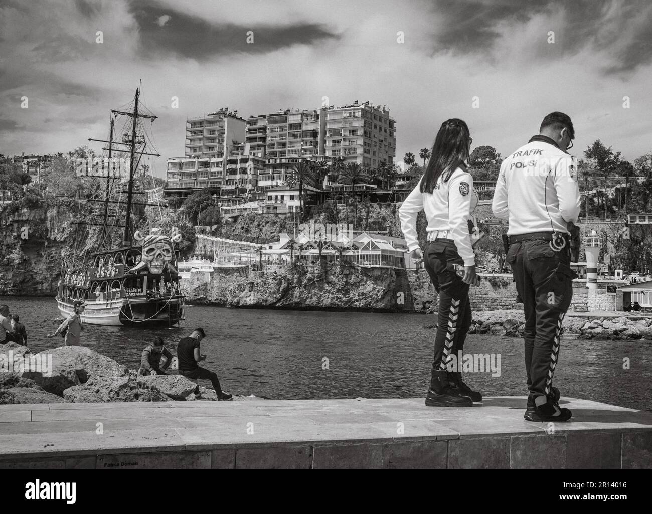 Un poliziotto e poliziotto si trovano ai margini dell'antico porto della città vecchia di Kaleici, Antalya, Turchia (Turkiye). Dietro di loro le persone si rilassano al Foto Stock