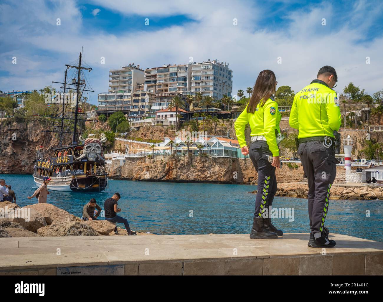 Un poliziotto e poliziotto si trovano ai margini dell'antico porto della città vecchia di Kaleici, Antalya, Turchia (Turkiye). Dietro di loro le persone si rilassano al Foto Stock