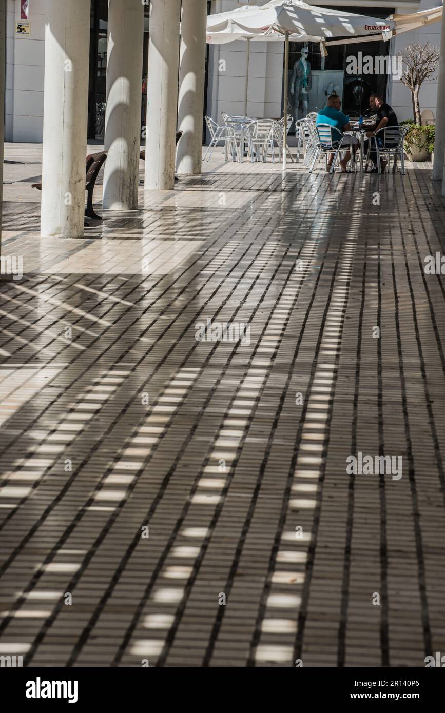 Due uomini si incontrano ad un tavolo da caffè all'ombra di una pergola in Plaza Antonio Banderas, Puerto Banus, Spagna Foto Stock