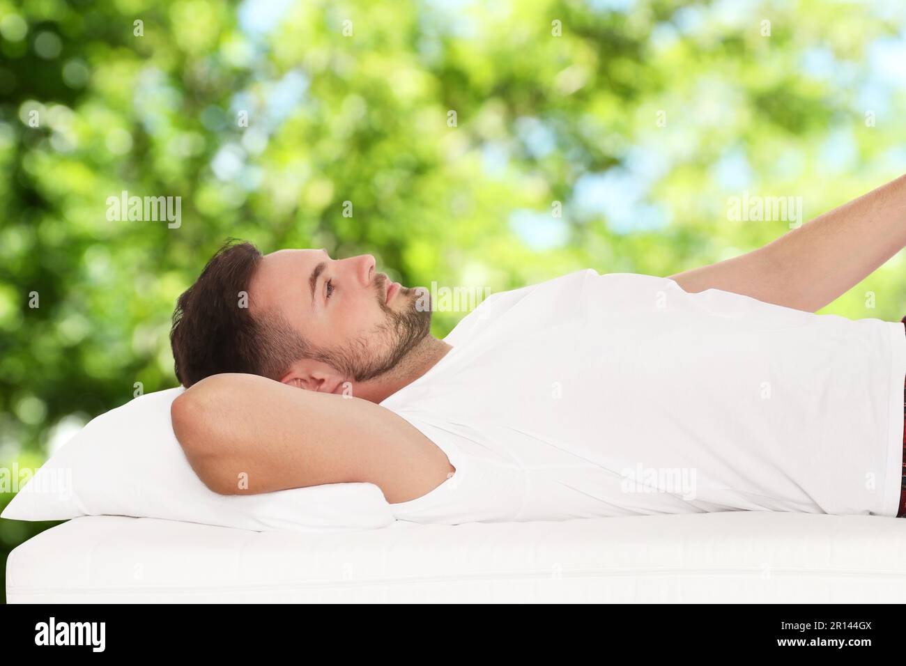 Uomo sdraiato su un comodo materasso su sfondo verde sfocato, effetto bokeh. Dormi bene - resta in salute Foto Stock