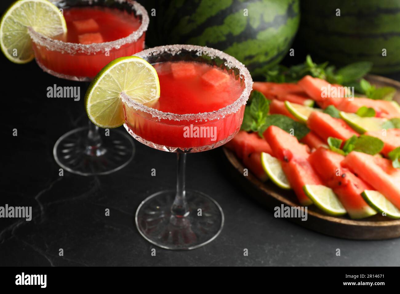 Bicchieri da cocktail di delizioso succo di cocomero fresco con lime e zucchero sul tavolo nero Foto Stock