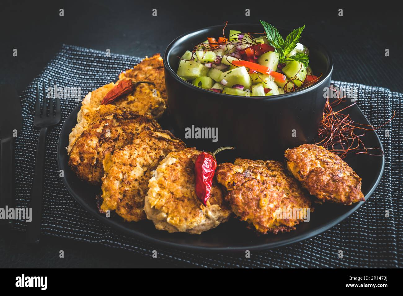 Insalata di cetrioli fresca in una ciotola nera con polpette di pesce o verdure o polpette intorno Foto Stock