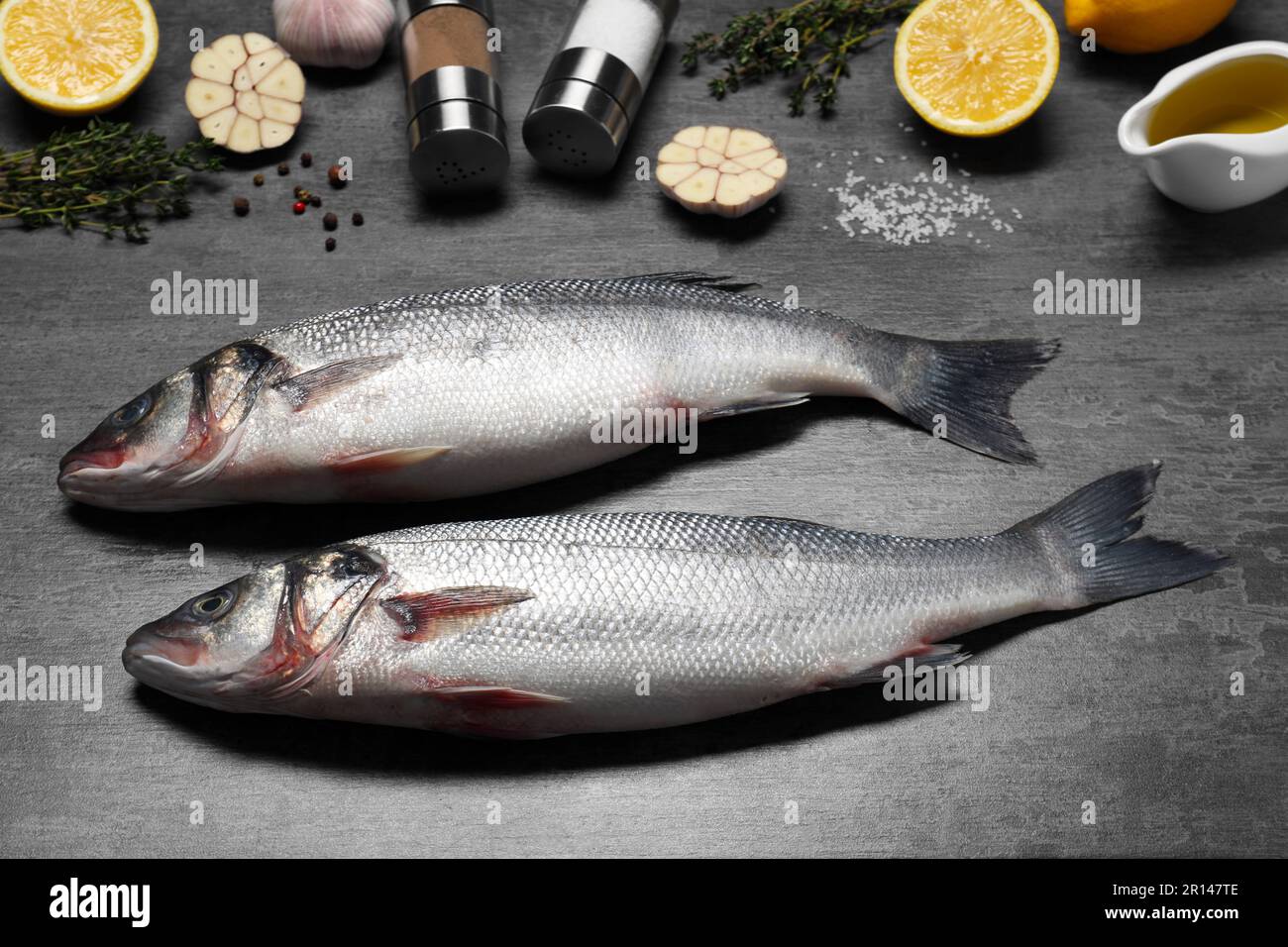 Pesce crudo fresco di spigola, condimenti e limoni su tavola nera Foto Stock