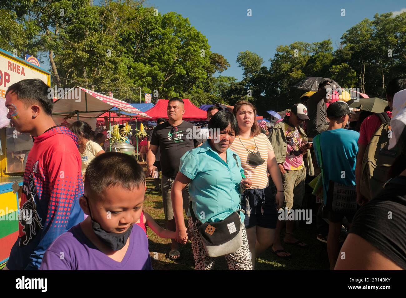 Malaybalay, Filippine - la donna tiene stretta la mano del bambino mentre cammina fra una folla della gente e le bancarelle colorate del cibo al festival di Kaamulan. Foto Stock