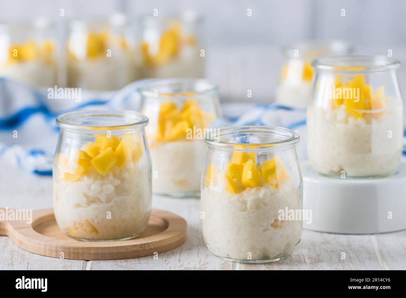 Budino di riso al cocco con mango in bicchieri da dessert su sfondo di legno bianco Foto Stock