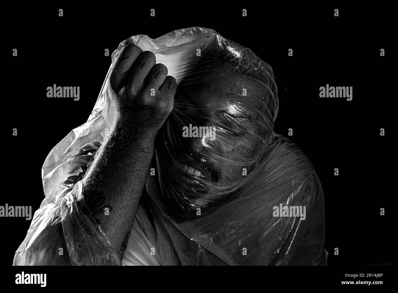 Uomo con sacchetto di plastica sopra la testa, soffocato. Scatto in bianco e nero. espressione del dolore. Foto Stock