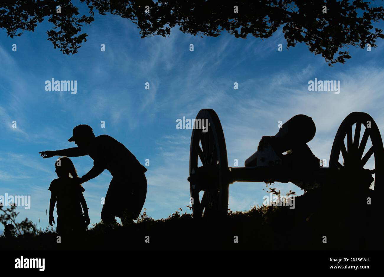 Il padre indica un oggetto di importanza storica per la sua giovane figlia in un parco commemorativo della guerra civile accanto a un antico canone Foto Stock