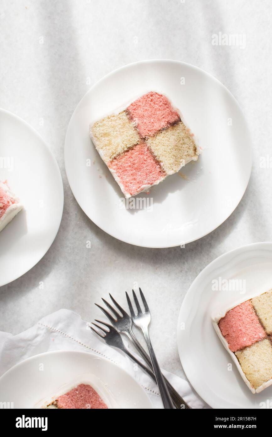 Vista dall'alto della fetta di torta di battenburg in un piatto bianco, torta di Spagna di mandorle e fragole ricoperta di fondente bianco, sezione trasversale di colore rosa e giallo Foto Stock