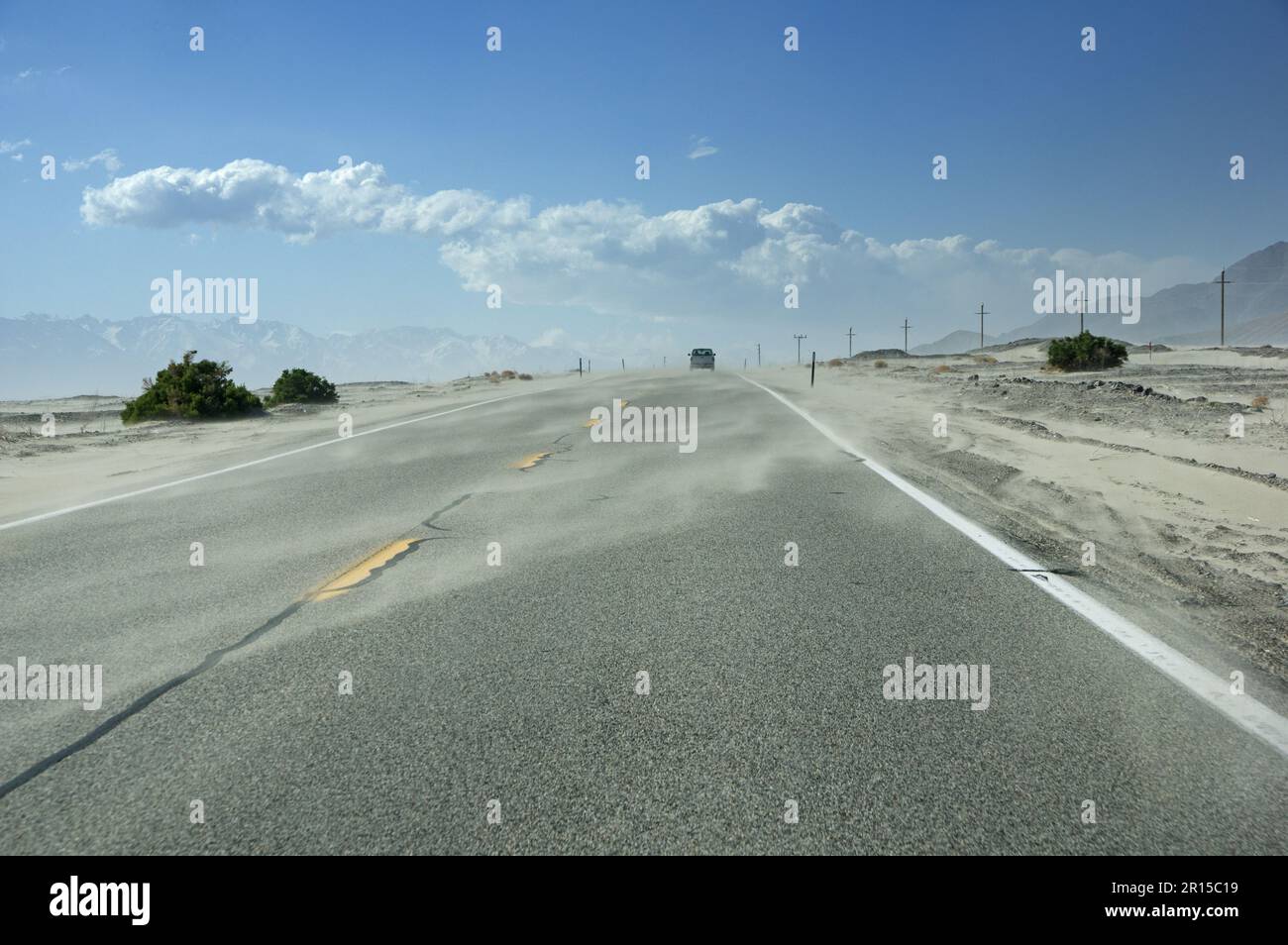 La sabbia soffia su una strada desertica di Owens Valley con un camion a distanza Foto Stock