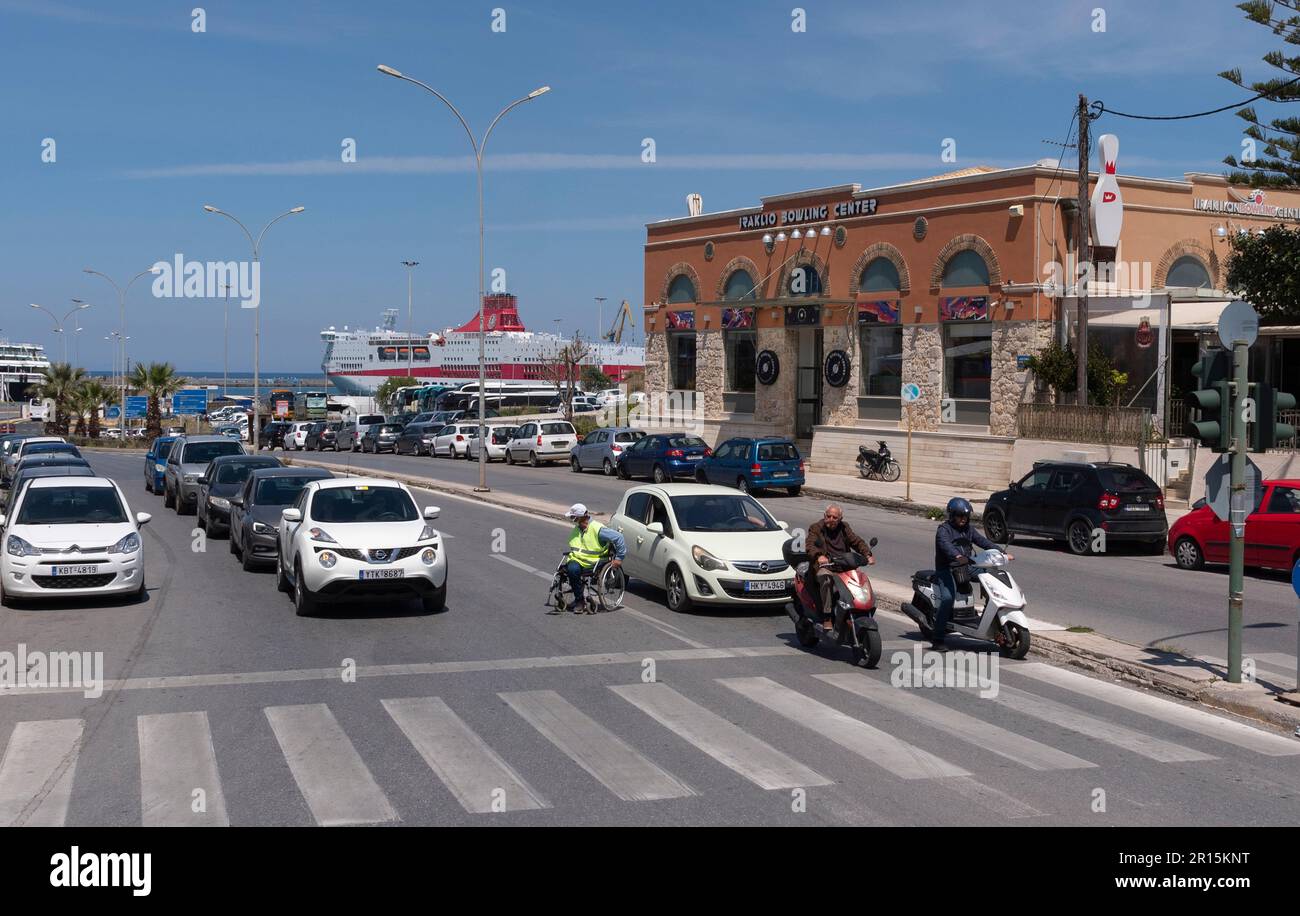 Candia, Creta, Grecia, UE. 2023. Persone disabili in sedia a rotelle tra le linee di traffico che tentano di attraversare la carreggiata nell'area portuale. Foto Stock