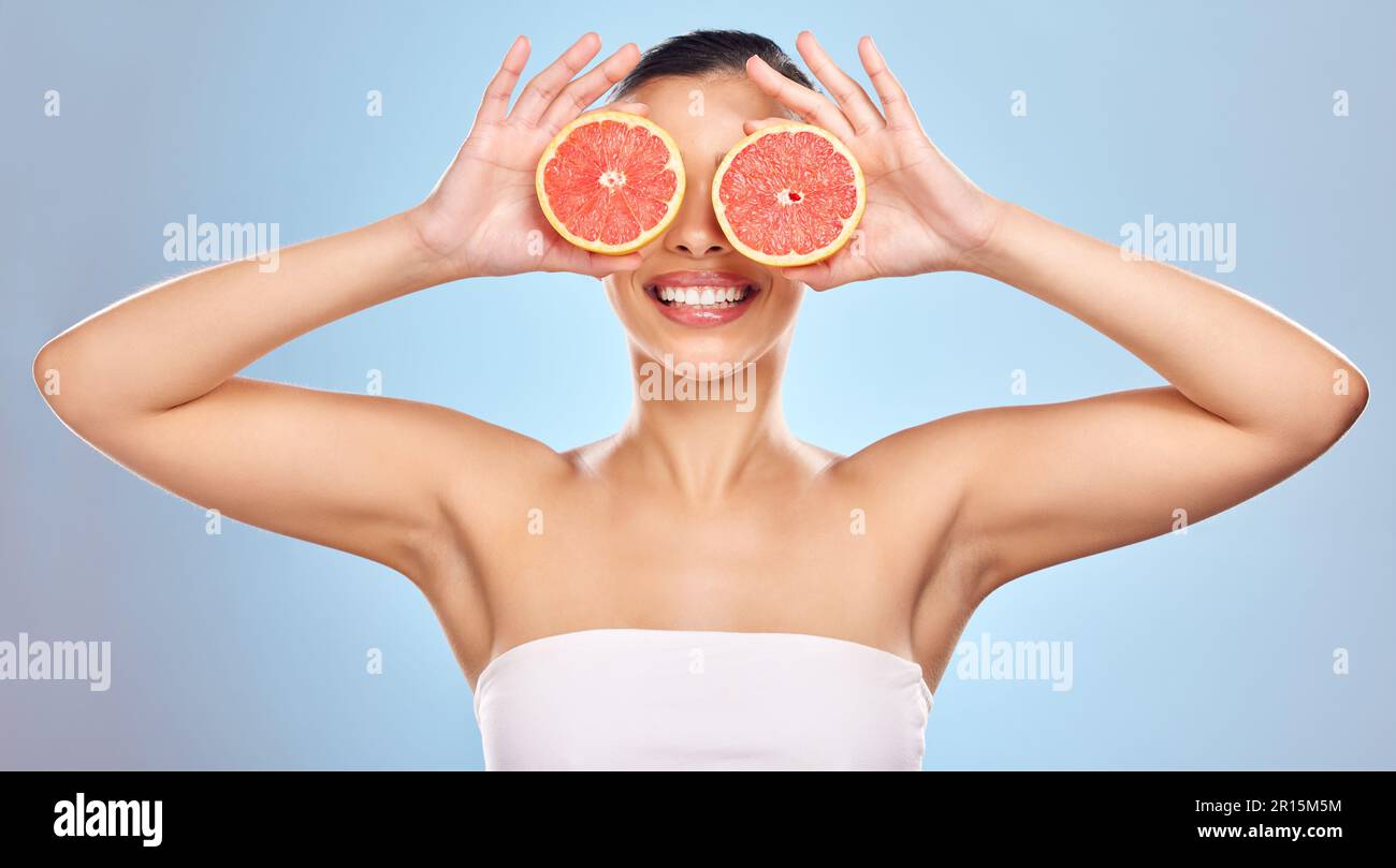 Pelle opacita con alcuni ingredienti naturali. Studio shot di una giovane donna attraente in posa con pompelmo su uno sfondo blu. Foto Stock