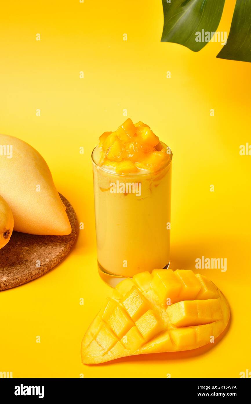 Succosa frullato di mango con fette di mango fresche su sfondo giallo. Bevande dolci di mango thailandesi. Concetto di bevande estive. Bevande gialle. Succo di frutta fresco Foto Stock