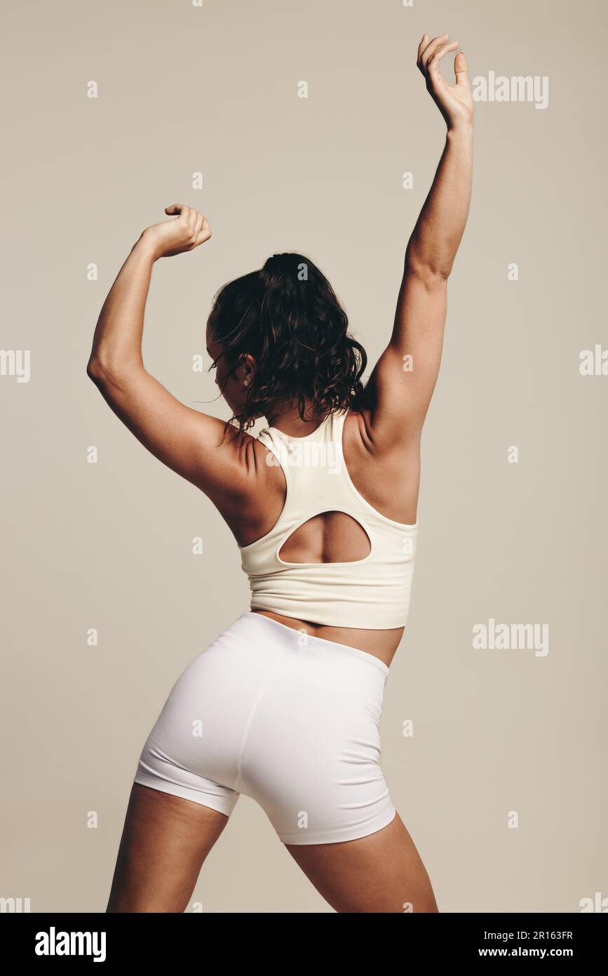 Un'atleta tonica e magra si alza in uno studio, eseguendo esercizi di tonificazione muscolare in abbigliamento sportivo. Donna che migliora il suo fitness fisico e flessibili Foto Stock