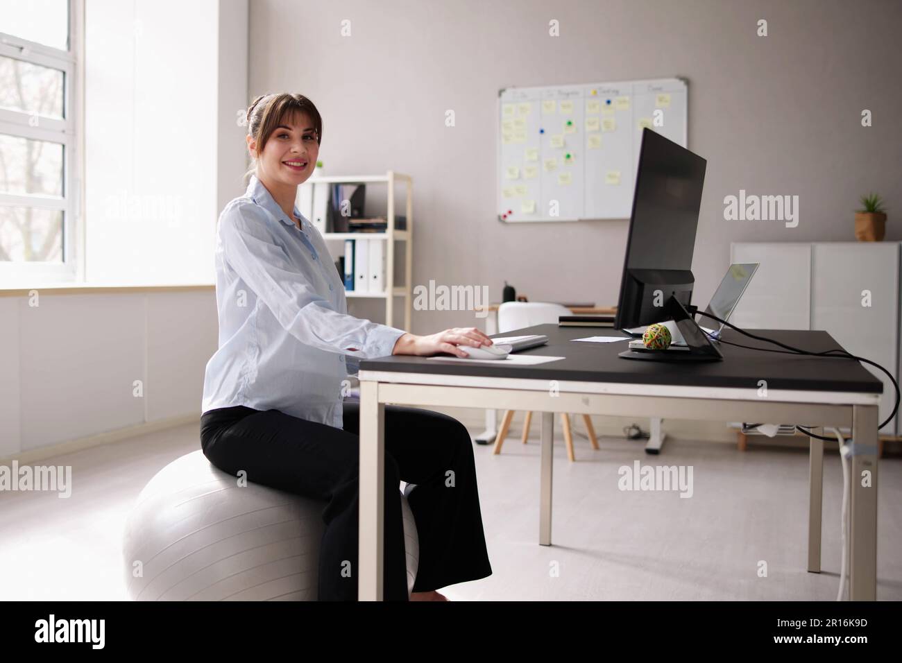Donna seduta sulla palla palestra in ufficio. Postura corretta Foto Stock