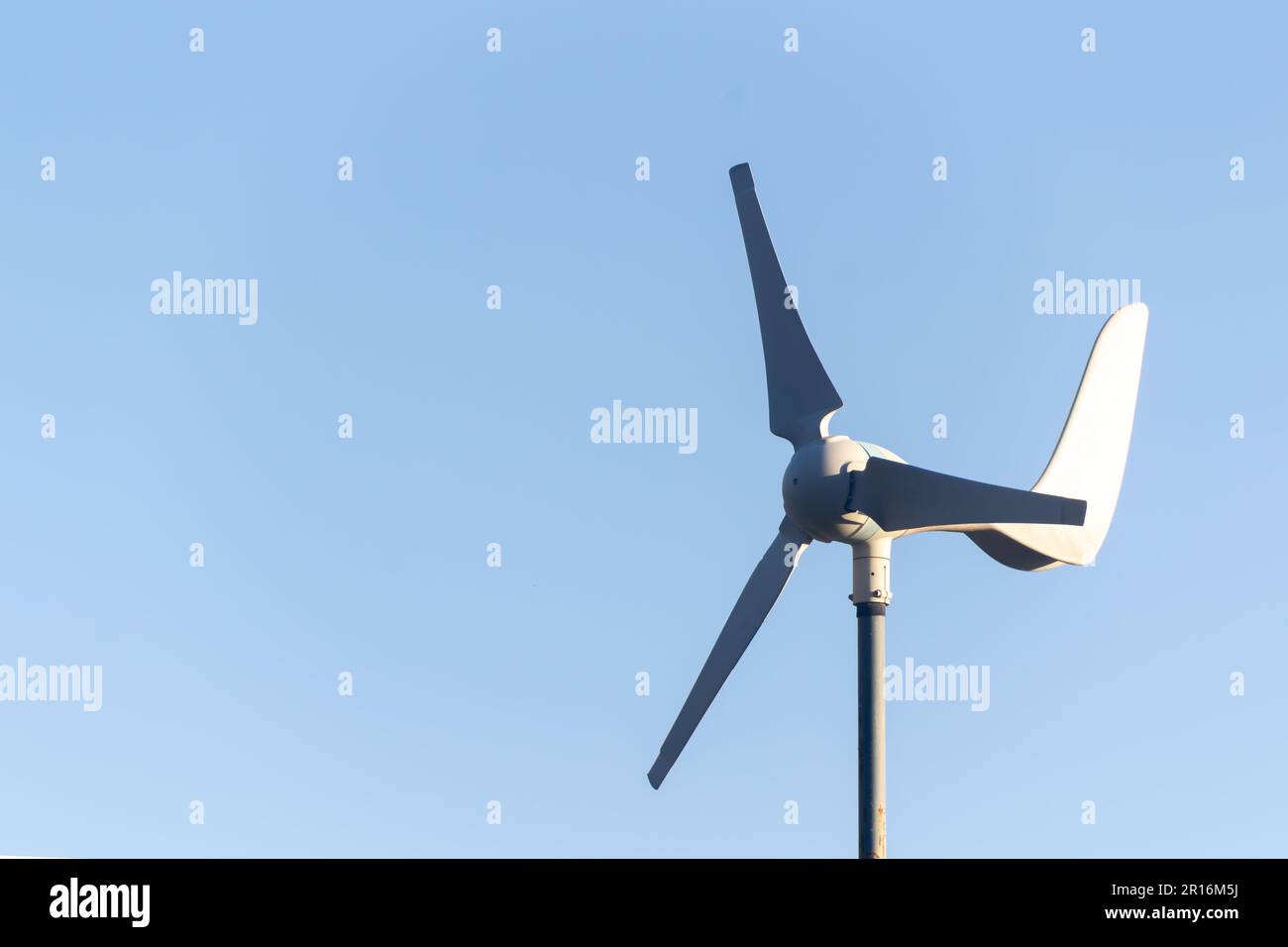 Dettaglio della testa di una piccola turbina eolica bianca con pale rotanti contro un cielo blu chiaro. Spazio per la copia disponibile sul lato sinistro del file IM Foto Stock Dettaglio della testa di una piccola turbina eolica bianca con pale rotanti contro un cielo blu chiaro. Spazio per la copia disponibile sul lato sinistro del file IM Foto Stock