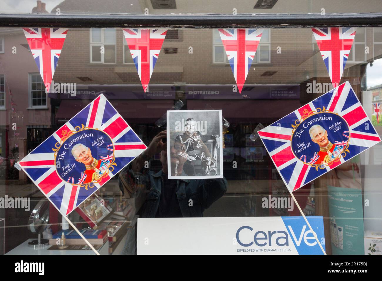 Celebrazioni per l'incoronazione reale e Union Jacks, e un ritratto di re Carlo 11, in una vetrina di farmacia a Londra, Inghilterra, Regno Unito Foto Stock