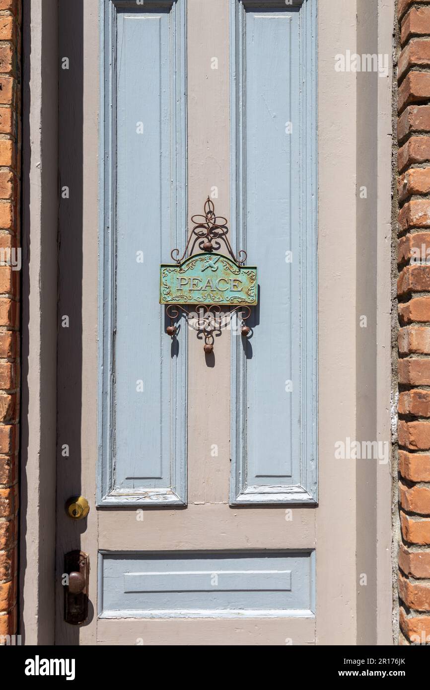 Vista ravvicinata di un'affascinante decorazione arrugginita con la parola 'PACE' appesa su una porta esterna in una giornata di sole Foto Stock