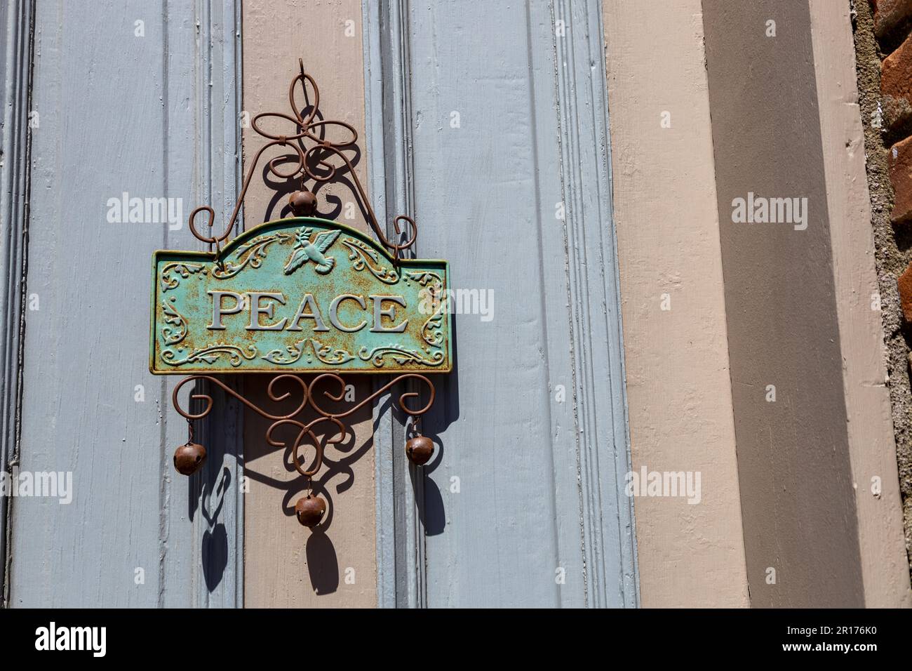 Vista ravvicinata di un'affascinante decorazione arrugginita con la parola 'PACE' appesa su una porta esterna in una giornata di sole Foto Stock