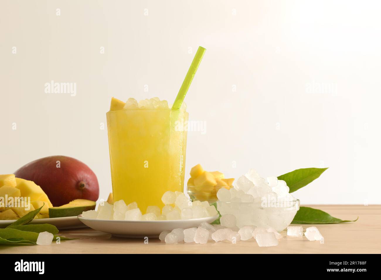 Particolare della bevanda di mango con molto ghiaccio su una panca di legno della cucina con la frutta e una ciotola con il ghiaccio intorno esso fondo isolato. Vista frontale. Orizzontale Foto Stock