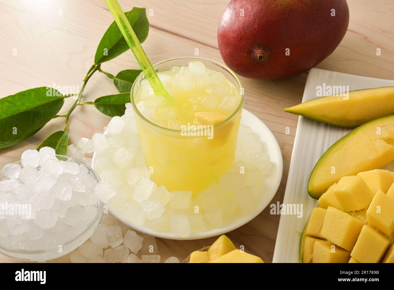 Particolare bicchiere con bevanda fredda di mango su piatto con ghiaccio e frutta intorno. Vista rialzata. Composizione orizzontale. Foto Stock