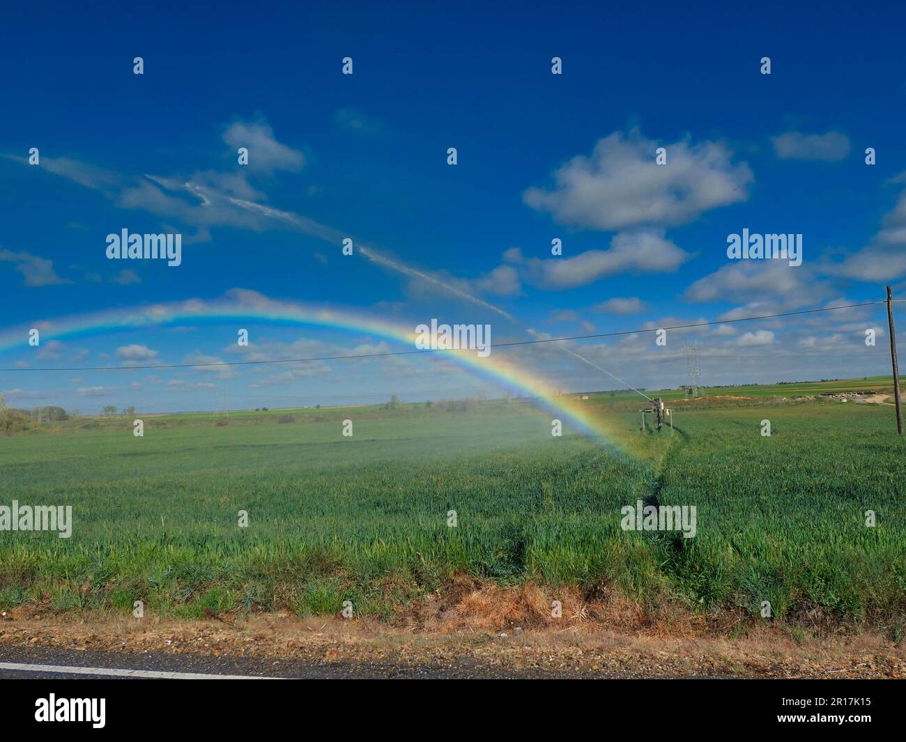 Arcobaleno causato dall'irroratrice dell'acqua agricola con campo verde Foto Stock