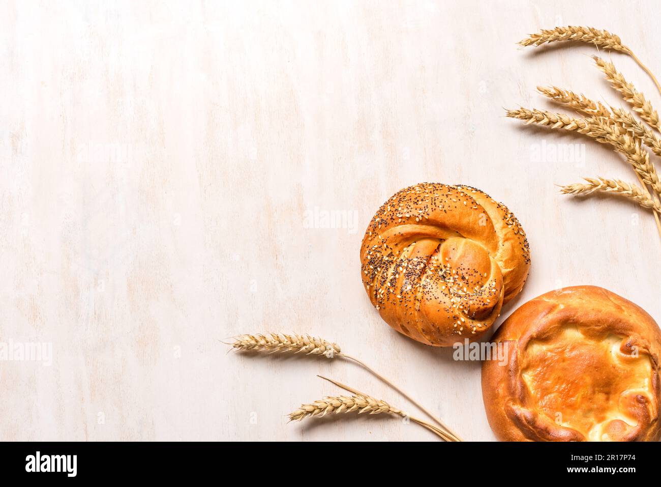 Spighe di grano e panini freschi su sfondo di legno bianco, spazio copia. Nuovo raccolto, pane cotto a casa e vacanza ebraica Shavuot concetto. Foto Stock