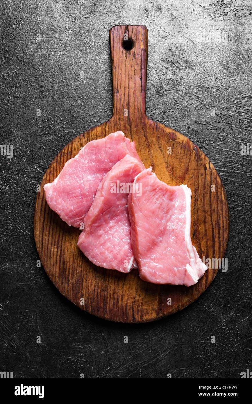 Fette di carne di maiale cruda sul tagliere, vista dall'alto. Pezzi di lombo di maiale. Foto Stock