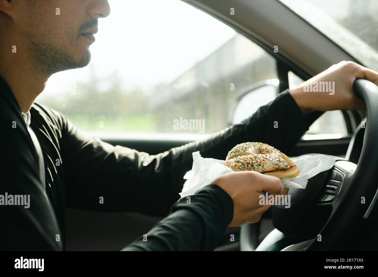 Uomo che tiene il sacchetto della colazione e guida in auto sulla strada per lavorare Foto Stock