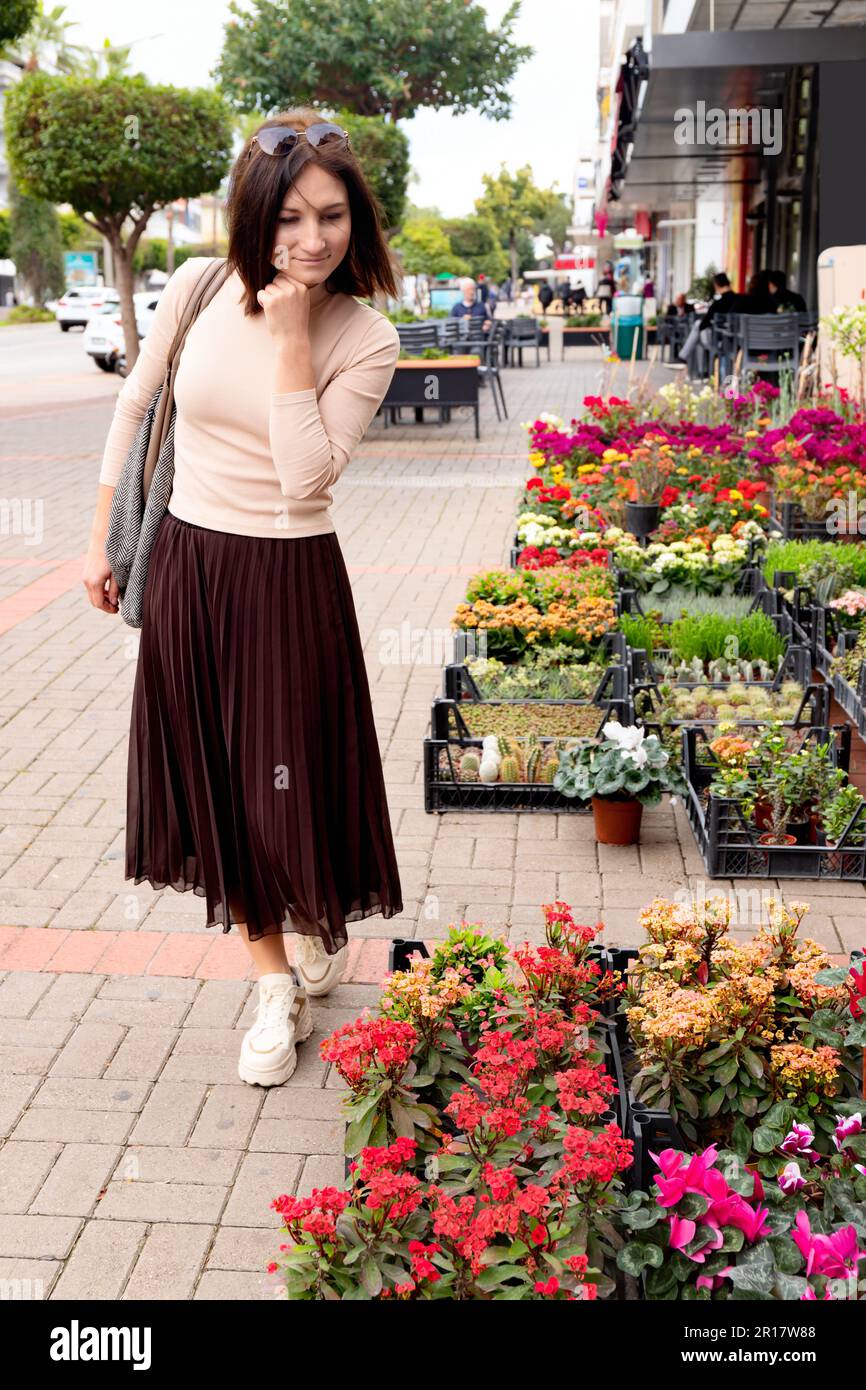Giovane donna che cammina lungo il negozio di fiori di strada. Foto Stock