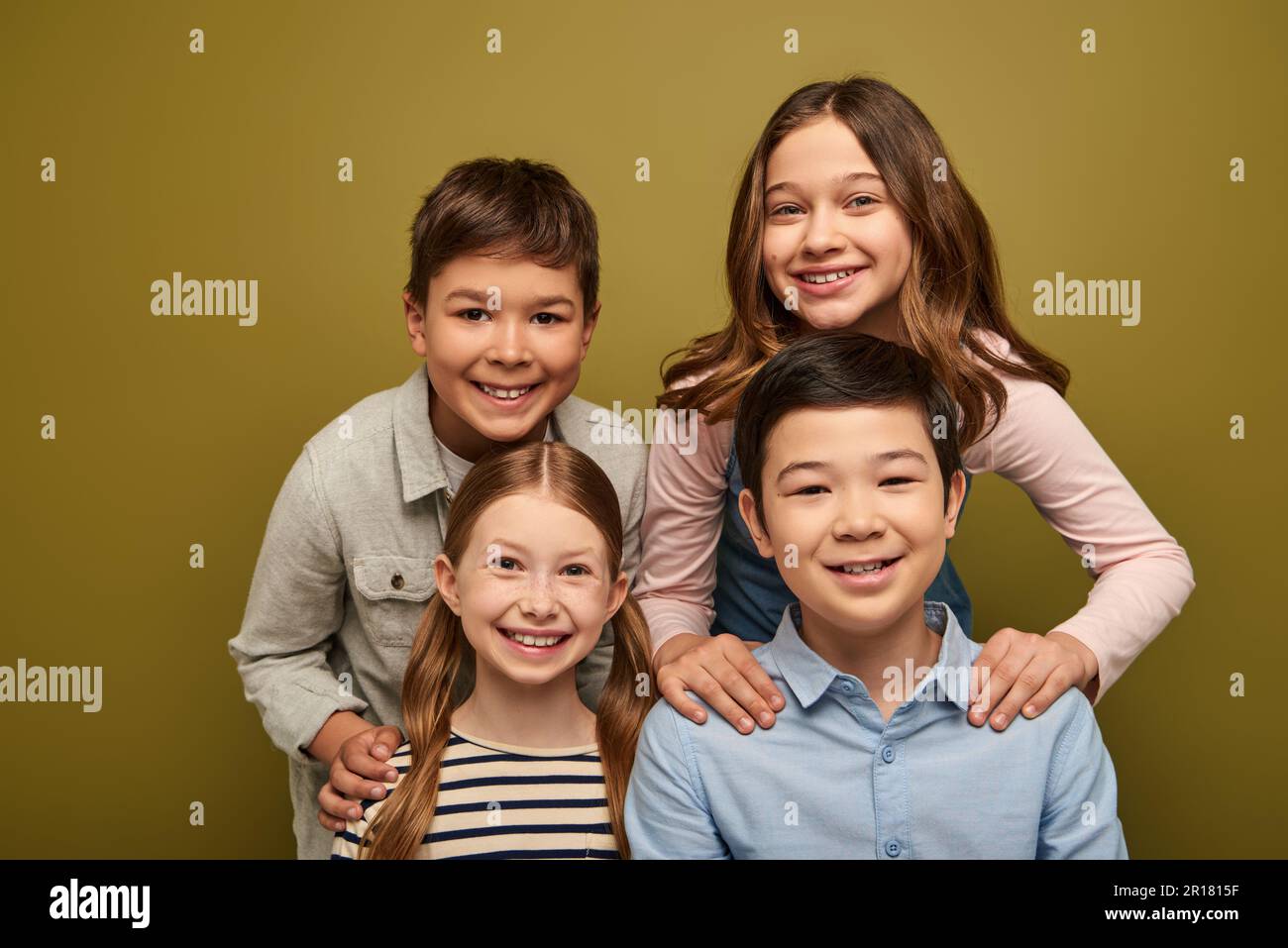 Felici bambini in abiti casual abbracciando gli amici e guardando la macchina fotografica mentre festeggia la giornata internazionale di protezione dei bambini su sfondo cachi Foto Stock