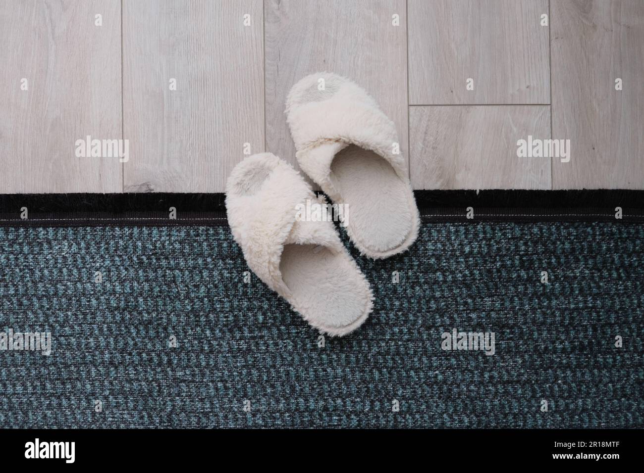 Soffici pantofole bianche che si trovano al centro di moquette e parquet. Concetto minimalista. Foto Stock