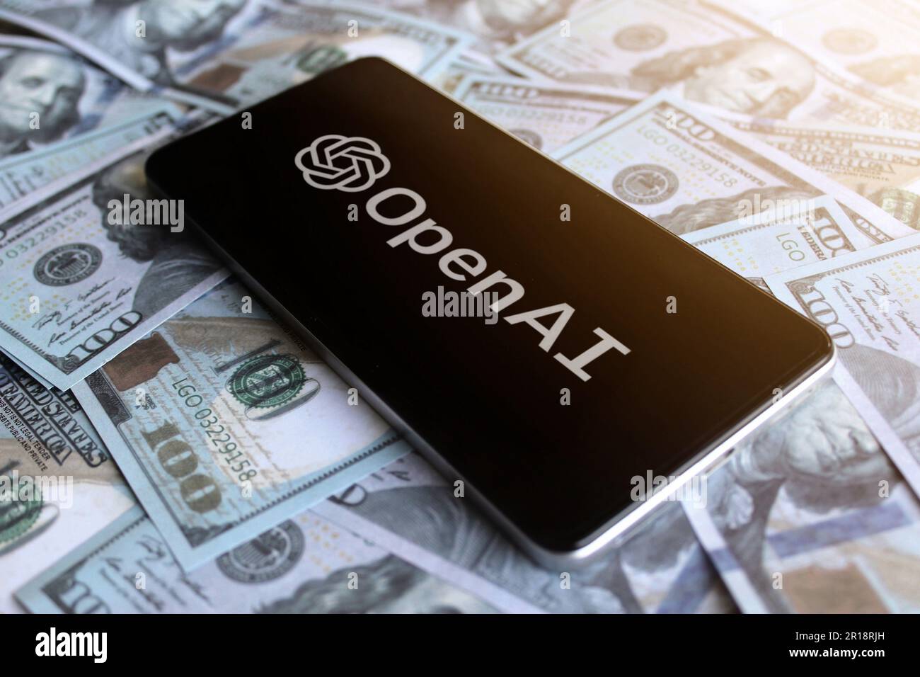 Logo OpenAI visualizzato sullo smartphone in cima a una pila di soldi. Foto Stock