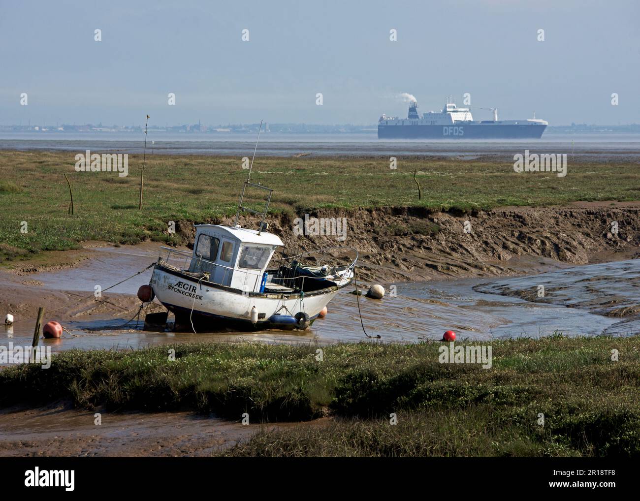 Barca da pesca con bassa marea a Stone Creek (con nave da carico in distanza), a Fonded Island, East Yorkshire, Inghilterra UK Foto Stock