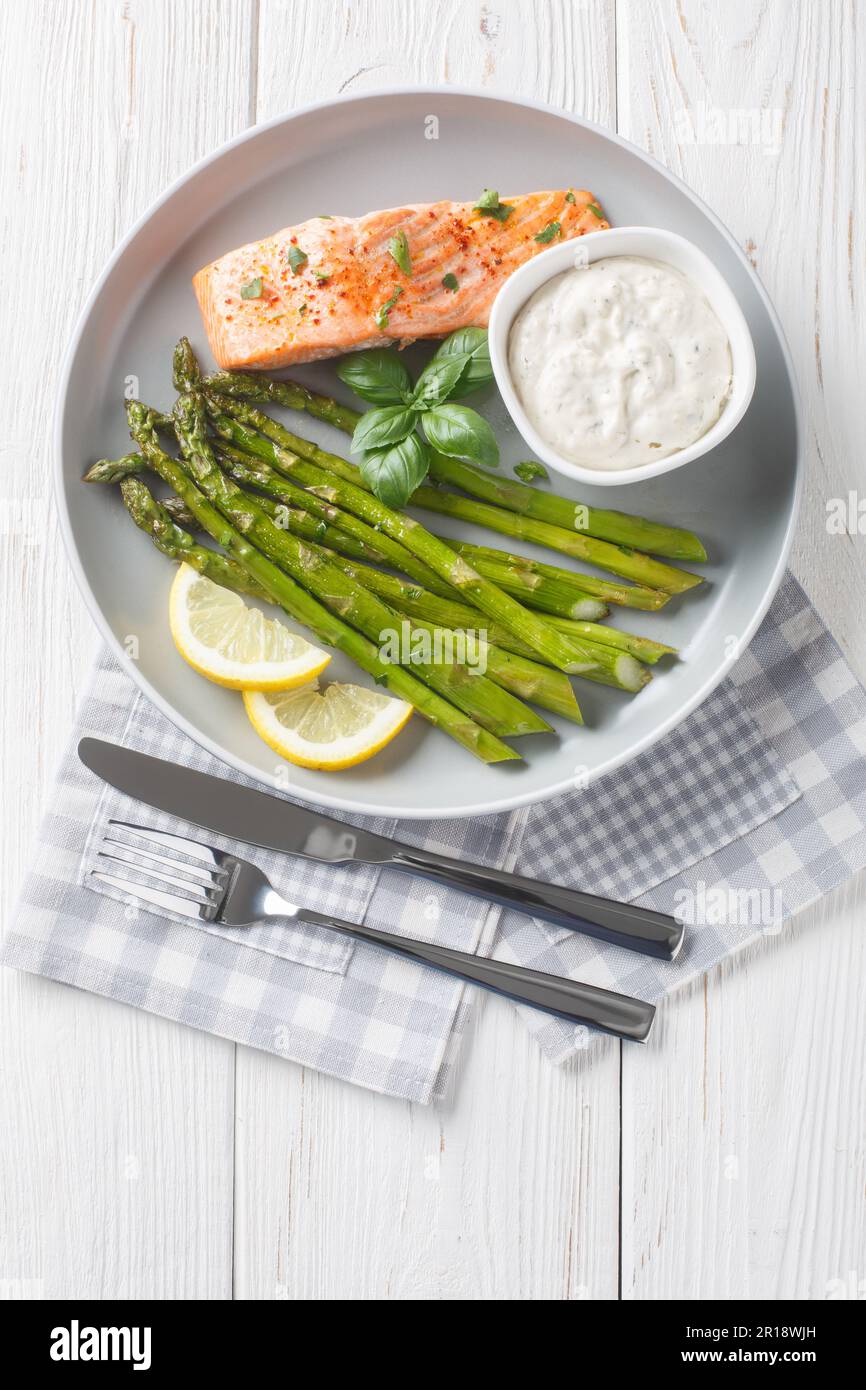 Filetto di salmone al forno con asparagi servito con salsa tartara e primo piano al limone in un piatto sul tavolo. Verticale dall'alto Foto Stock