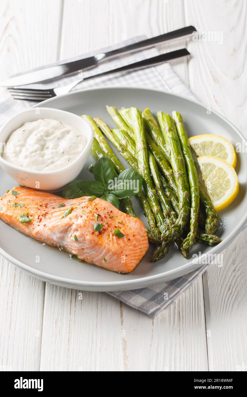 Filetto di salmone al forno con asparagi servito con salsa tartara e primo piano al limone in un piatto sul tavolo. Verticale Foto Stock