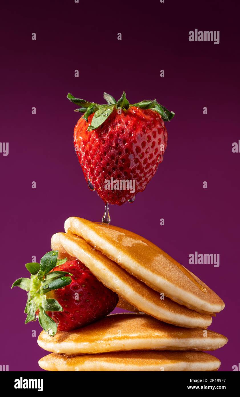 Levitating fragola su una pila di frittelle gocciolate con miele. Ripresa concettuale. Foto Stock