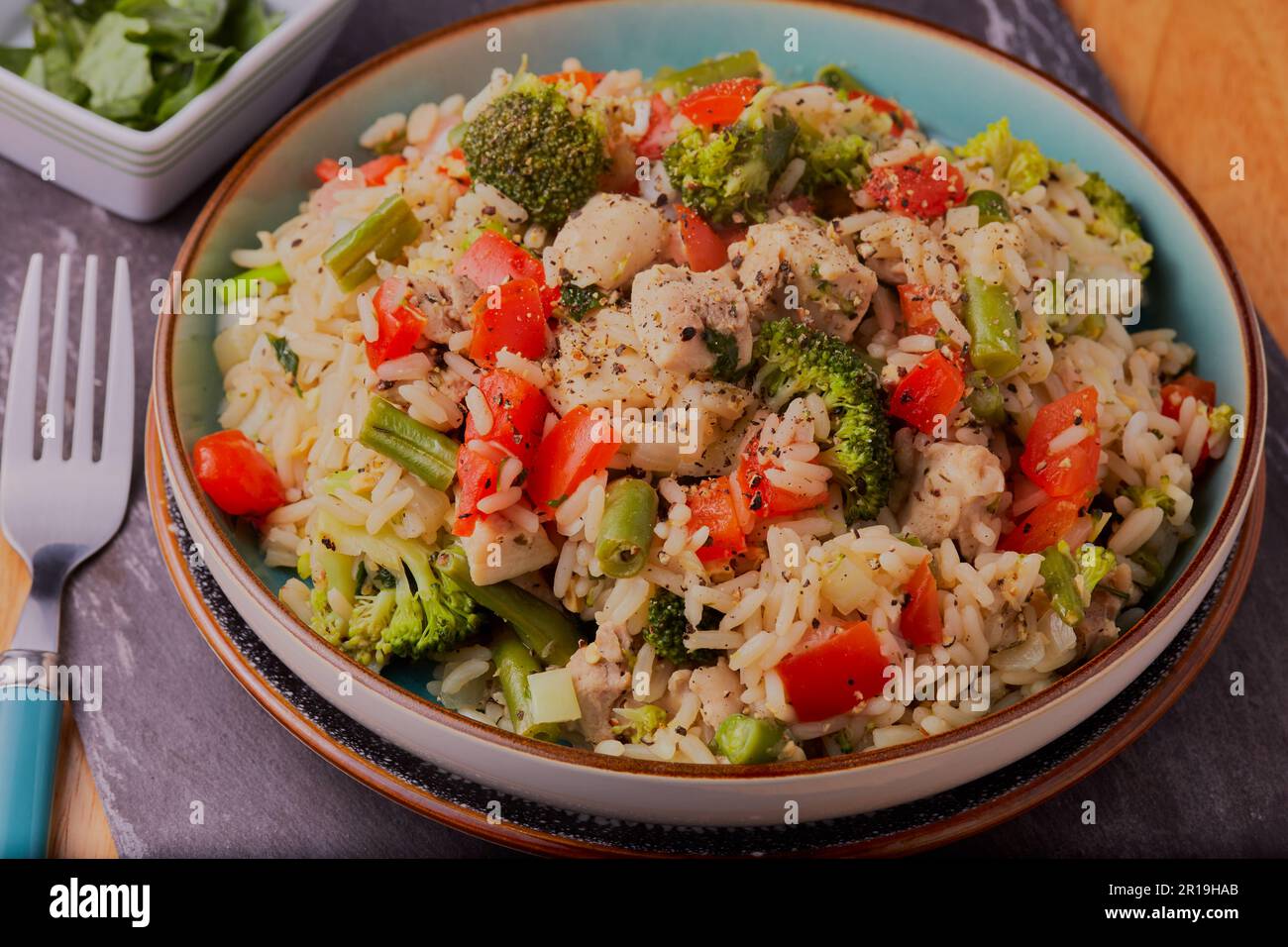 Pasto sano di pollo con riso e verdure e guarnito con condimento ed erbe aromatiche. Foto Stock