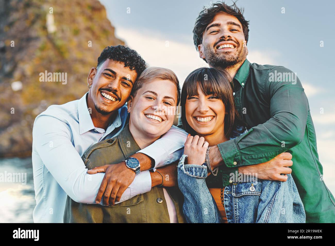 Ritratto di quattro amici multiculturali che si abbracciano e si propongono per una foto sul lungomare, con un individuo che si identifica come non binario, s Foto Stock