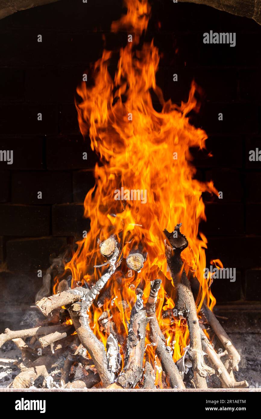 Un falò alto con linguette affilate di fiamme gialle e arancioni su uno sfondo di fumo scuro in muratura. Un forno per barbecue all'aperto. Preparazione di Foto Stock